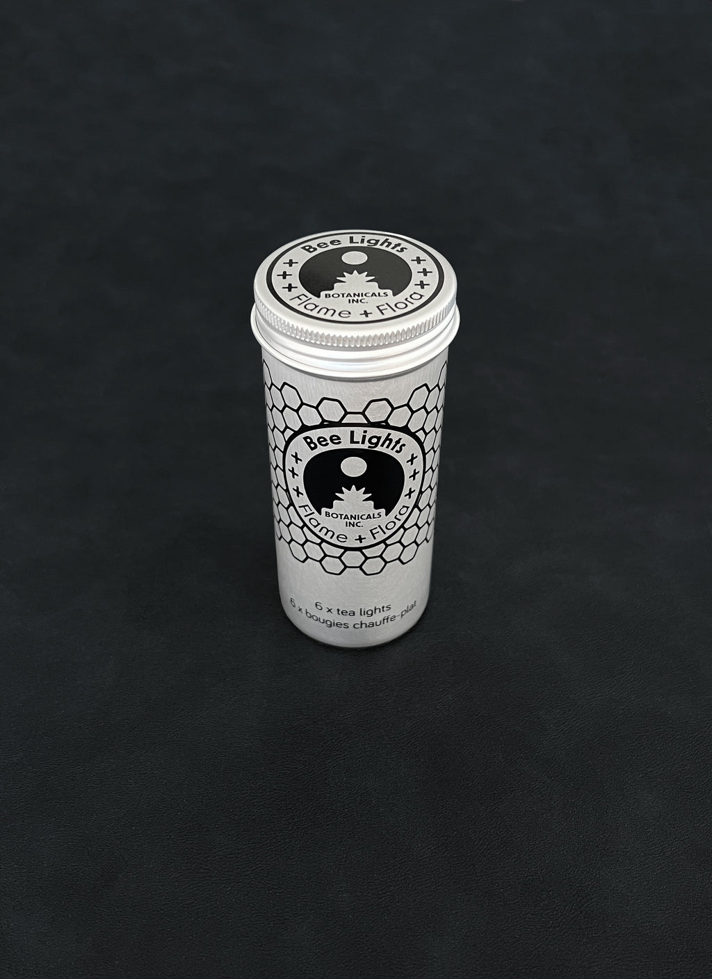 Silver metal storage tin with black patterned design for beeswax tealights on a dark background