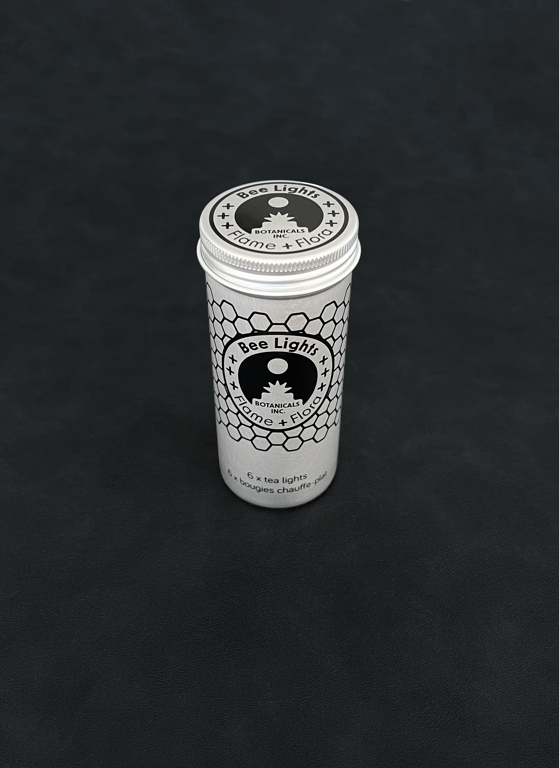 Silver metal storage tin with black patterned design for beeswax tealights on a dark background