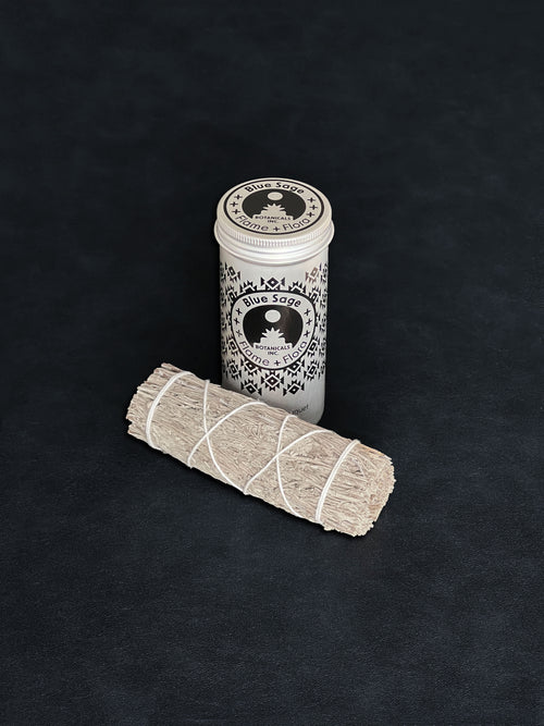 Blue Sage storage tin with black patterned design and a bundle of Blue Sage tied with white cotton string displayed in the foreground on a dark background