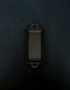 Bird’s-eye view of a rectangular black cast iron incense burner with handles on both ends in a vertical orientation against a dark background