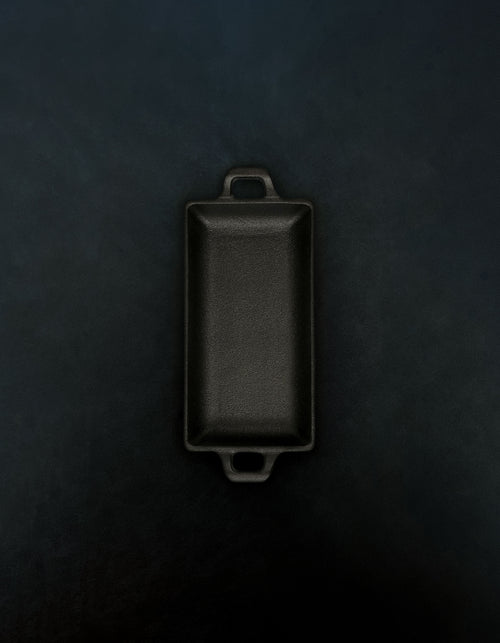 Bird’s-eye view of a rectangular black cast iron incense burner with handles on both ends in a vertical orientation against a dark background