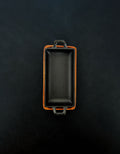 Bird’s-eye view of a rectangular black cast iron incense burner in a vertical orientation with handles on both ends, nested in an acacia wood tray against a dark background