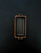 Bird’s-eye view of a rectangular black cast iron incense burner in a vertical orientation with handles on both ends, nested in an acacia wood tray against a dark background