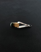 Metal tongs holding a charred stick of Palo Santo on a dark background