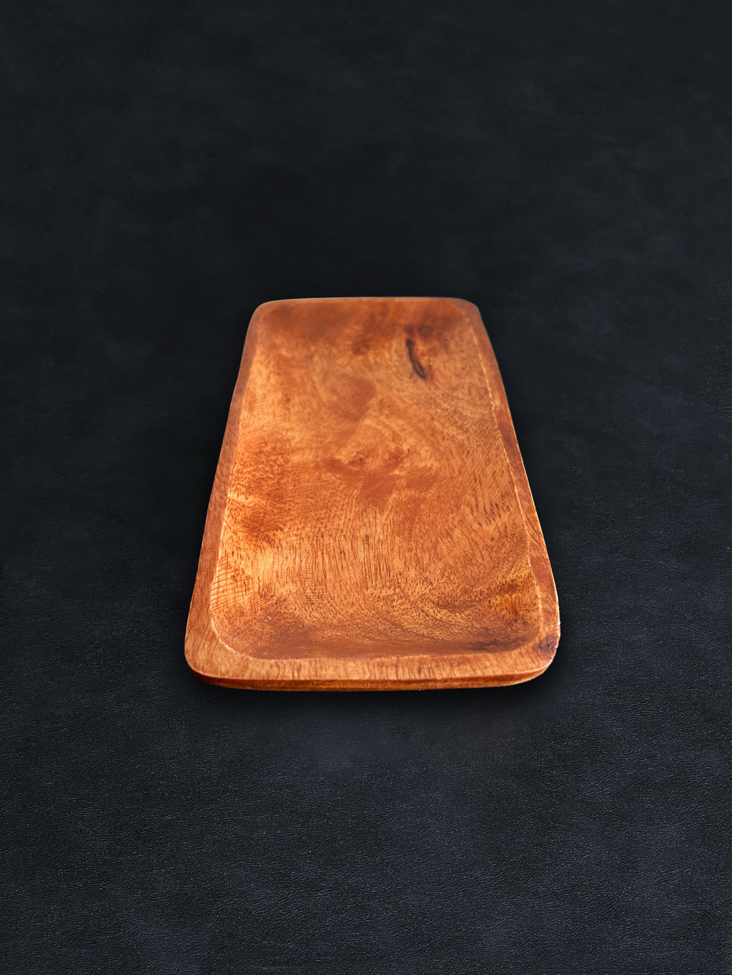 A rectangular acacia wood tray positioned vertically on a dark surface