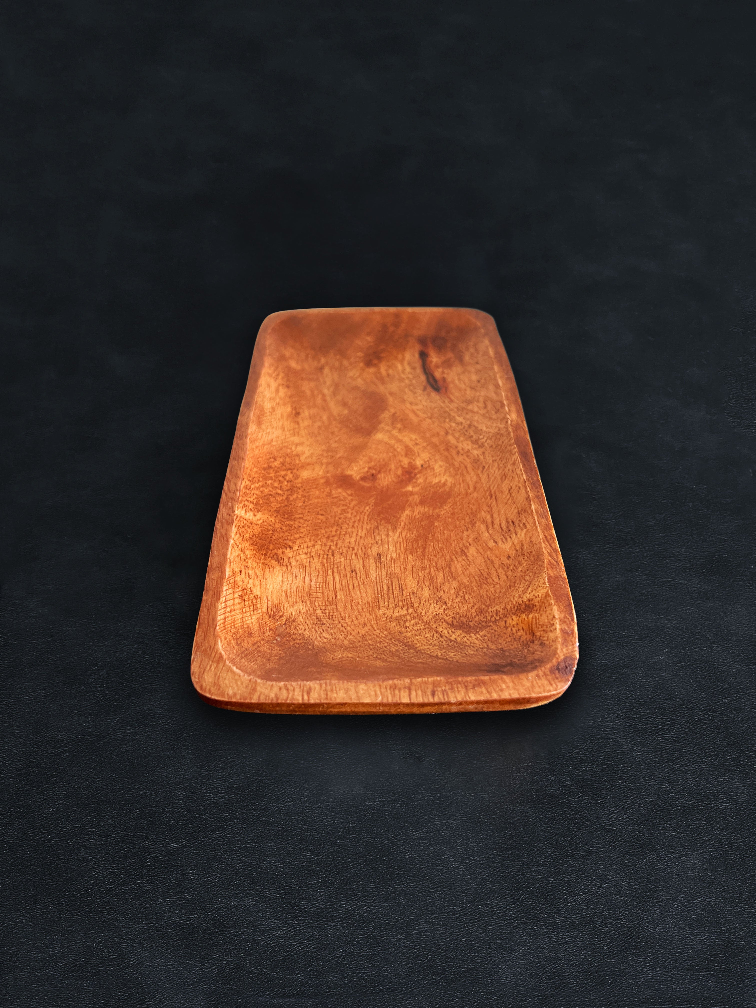 A rectangular acacia wood tray positioned vertically on a dark surface