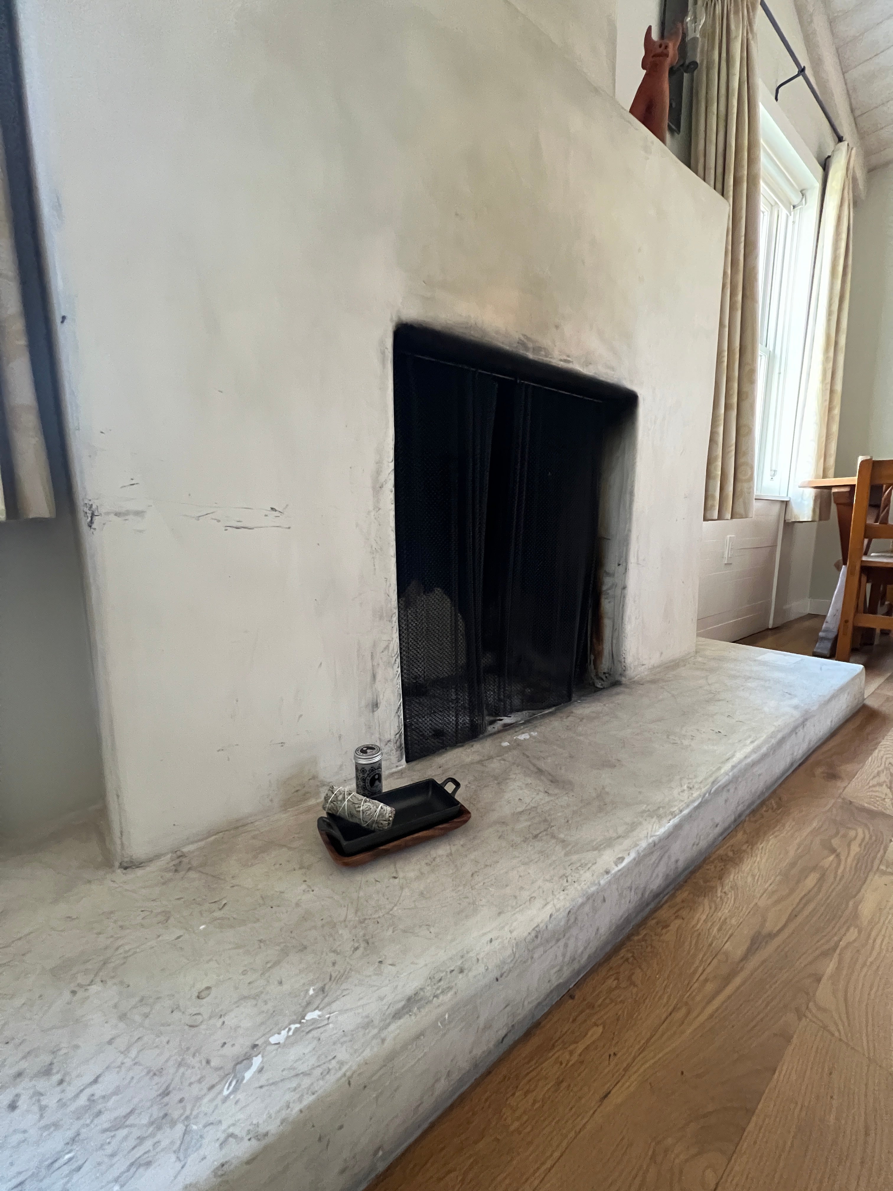 White sage storage tin with black patterned design and white sage bundle tied with cotton string shown in a cast iron incense burner and acacia wood tray set on a concrete fireplace