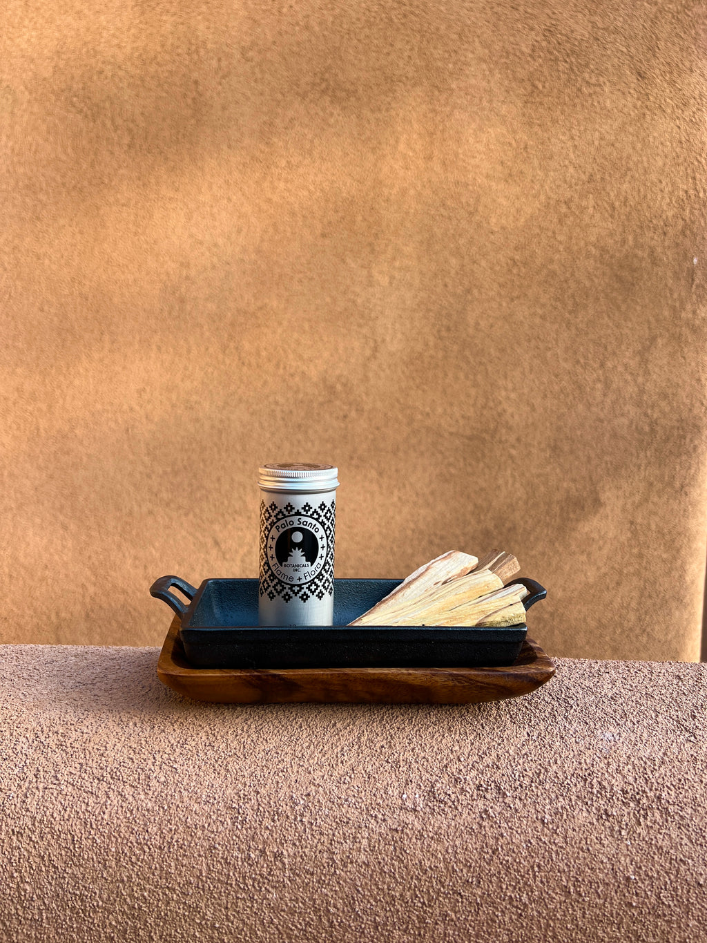 Palo Santo storage tin with cast iron incense burner and acacia wood tray holding Palo Santo sticks on a beige adobe-style garden wall in a styled outdoor setting