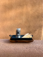 Palo Santo storage tin with cast iron incense burner and acacia wood tray holding Palo Santo sticks on a beige adobe-style garden wall in a styled outdoor setting