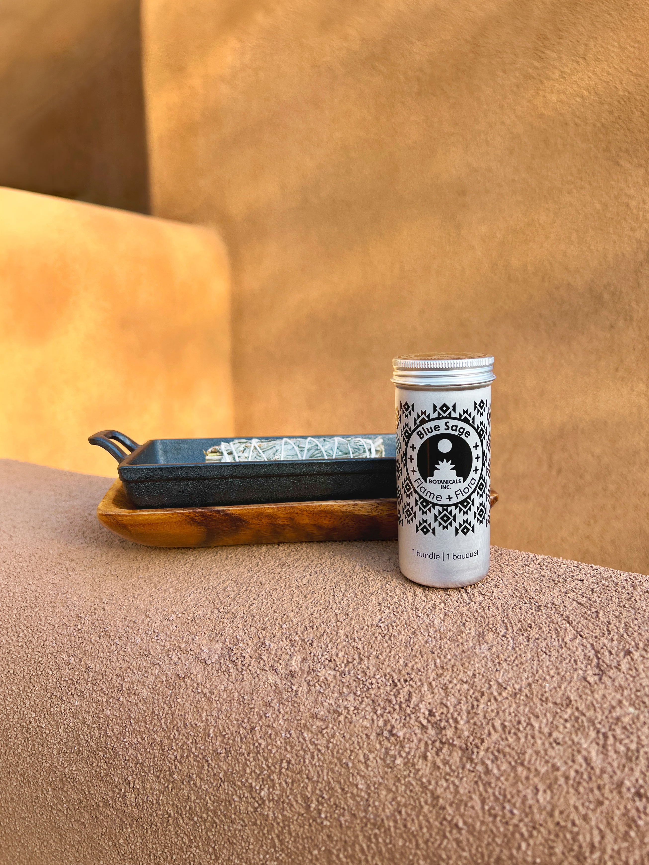 Blue Sage storage tin with cast iron incense burner and acacia wood tray holding Blue Sage tied with white cotton string on a beige adobe-style garden wall in a styled outdoor setting