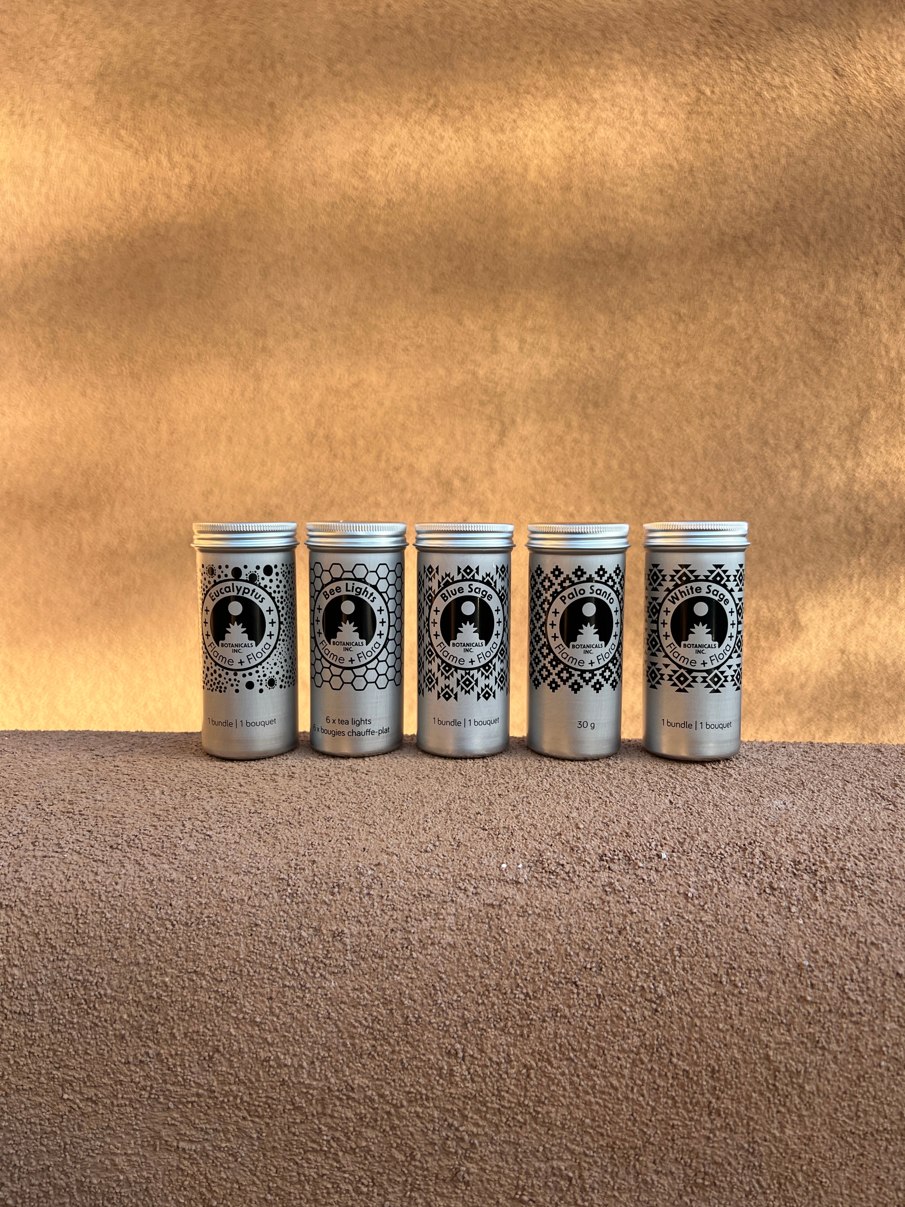 Five silver cans with black labels on a textured adobe ledge with an adobe wall background.