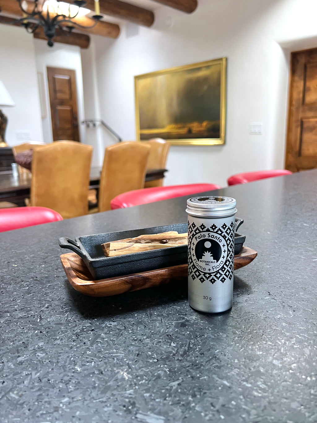 Palo santo storage tin with black pattern design alongside cast iron incense burner and acacia wood tray holding palo santo sticks in a styled dining room setting