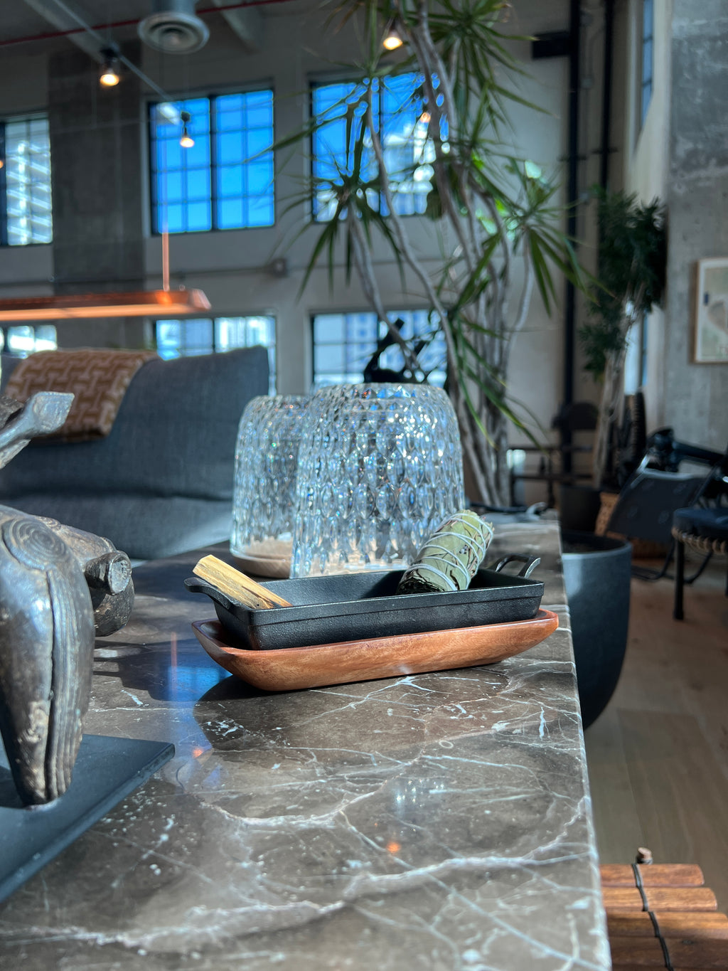 Cast iron incense burner and acacia wood tray set holding a bundle of Eucalyptus tied with white cotton string and a stick of Palo Santo on a dark marbled surface in a styled living room
