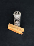 Palo Santo storage tin with black patterned design and four palo santo sticks displayed in the foreground on a dark background