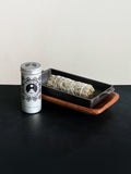 White Sage storage tin with black patterned design and a bundle of White Sage tied with white cotton string displayed with a cast iron incense burner and acacia wood tray set on a black surface against a white background