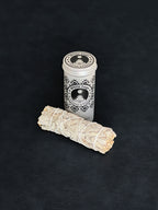 White Sage storage tin with black patterned design and a bundle of White Sage tied with white cotton string displayed in the foreground on a dark background