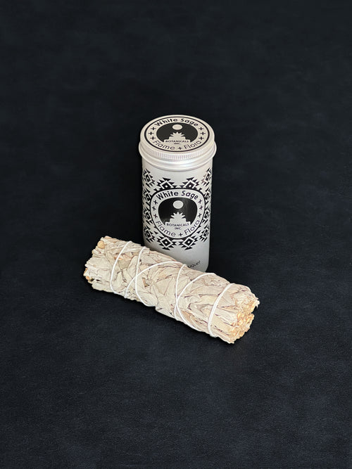 White Sage storage tin with black patterned design and a bundle of White Sage tied with white cotton string displayed in the foreground on a dark background