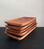 Stack of rectangular acacia wood trays positioned at an angle on a dark surface against a white background