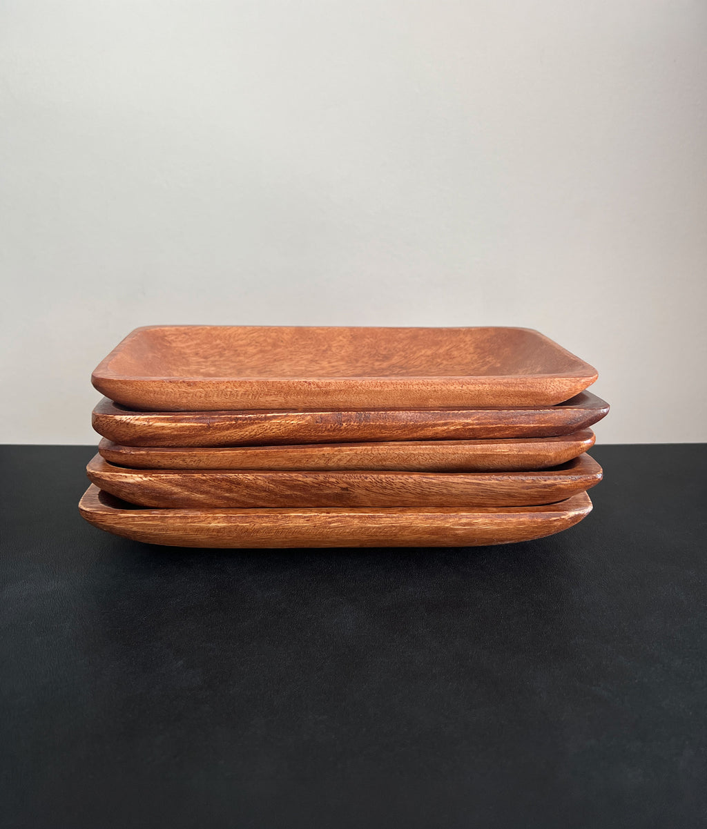 Stack of rectangular acacia wood trays positioned horizontally on a dark surface against a white background