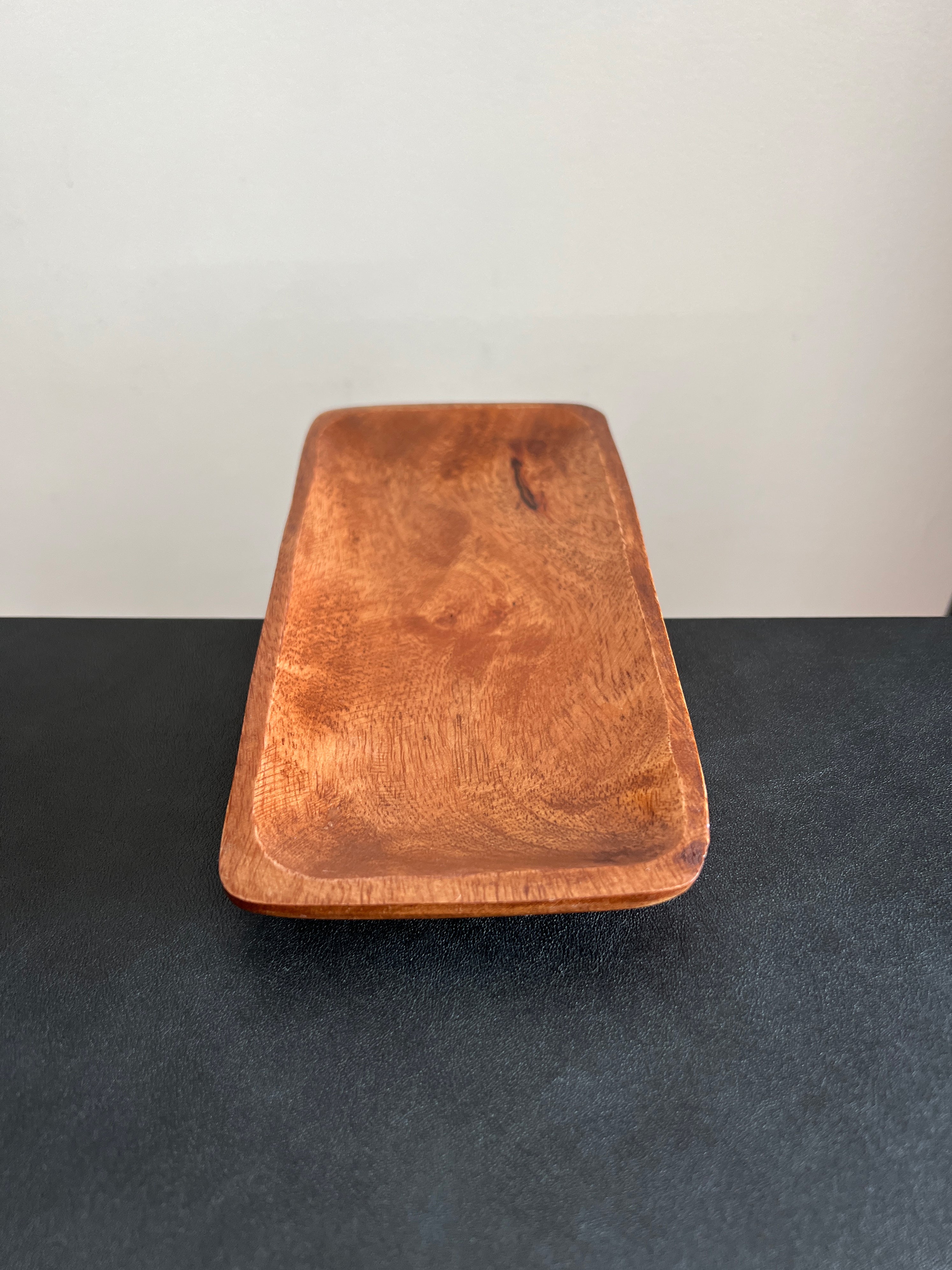 A rectangular acacia wood tray positioned vertically on a dark surface against a white background