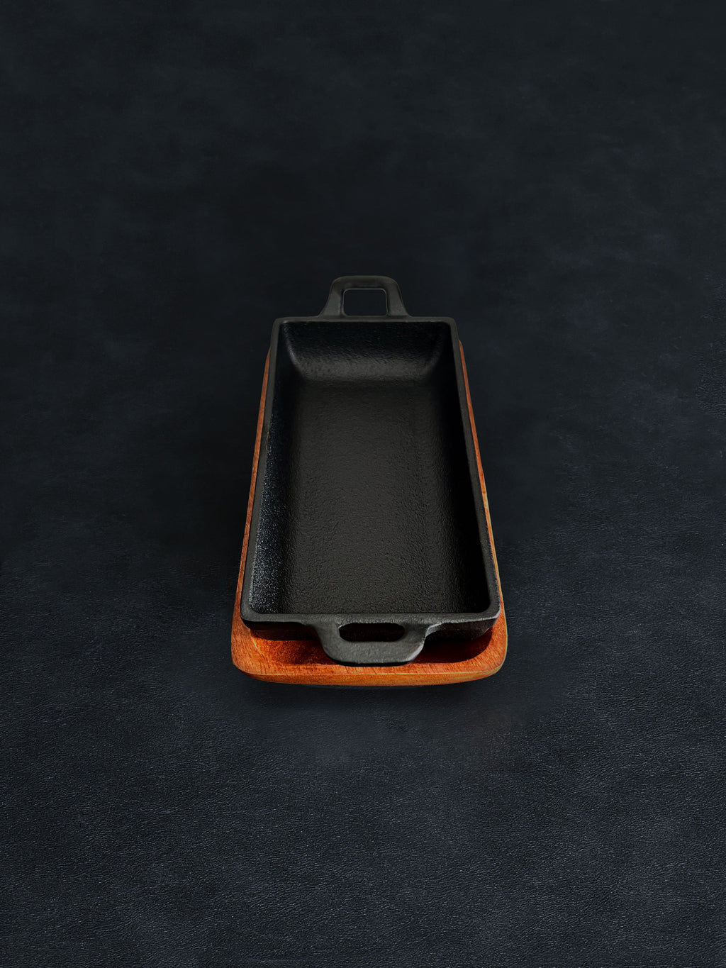 Bird’s-eye view of a rectangular black cast iron incense burner in a vertical orientation with handles on both ends, nested in an acacia wood tray on a dark surface against a white background