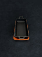 Bird’s-eye view of a rectangular black cast iron incense burner in a vertical orientation with handles on both ends, nested in an acacia wood tray on a dark surface against a white background